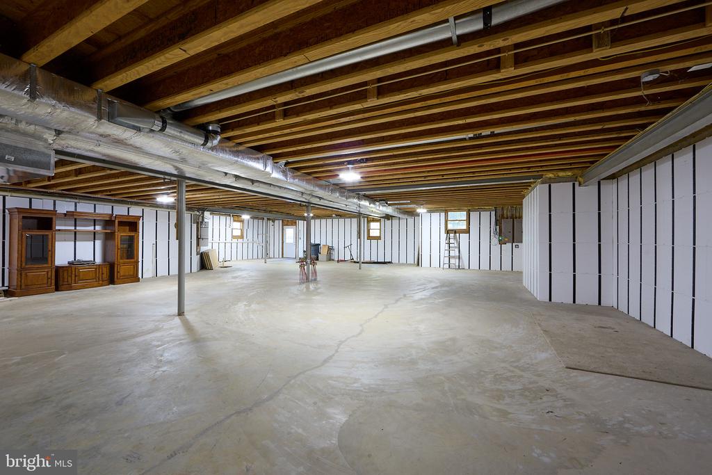 Unfinished basement with a broad concrete floor, exposed ceiling joists, and visible ductwork.