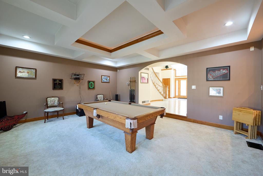 Billiards room with a wooden pool table, tray ceiling, and arched opening to a bright foyer.