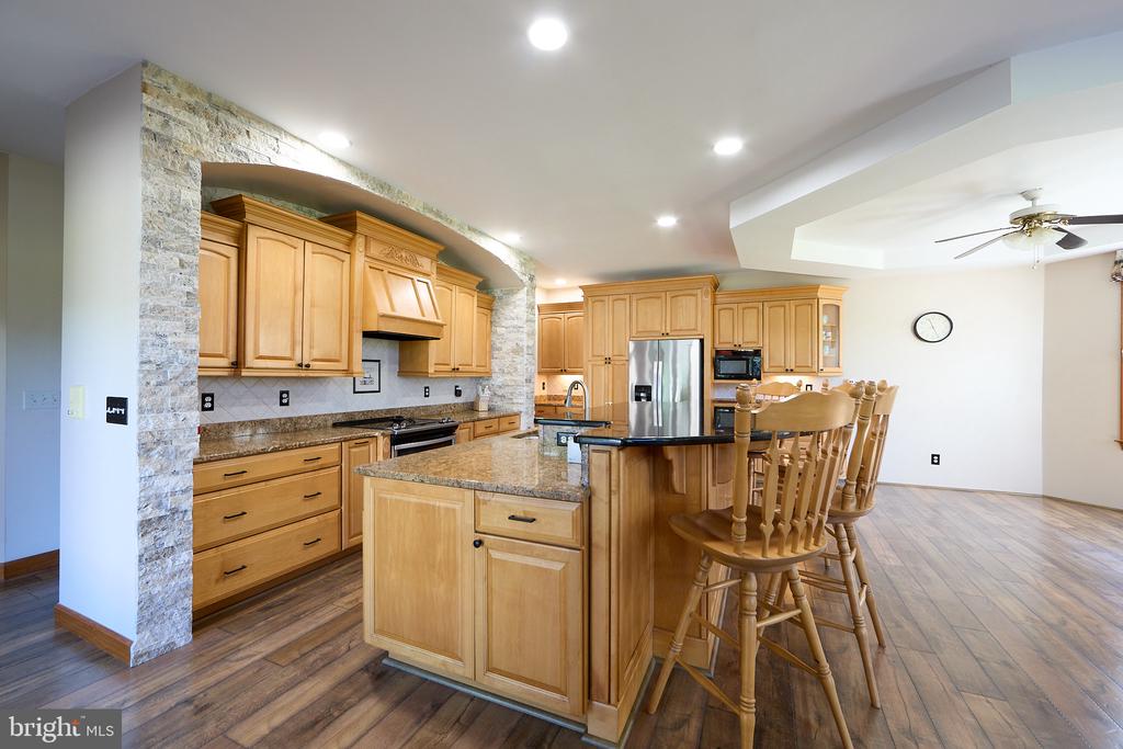 Kitchen with honey-colored cabinets, stone counters, a central island, and a breakfast bar with wooden stools.