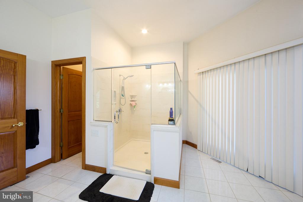 Bathroom with a glass-enclosed walk-in shower, white tile flooring, and vertical blinds.