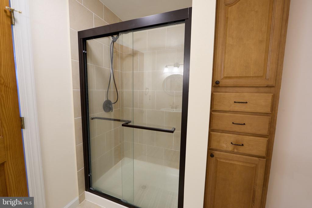Tiled bathroom shower with a dark-framed glass enclosure beside built-in wooden cabinetry.
