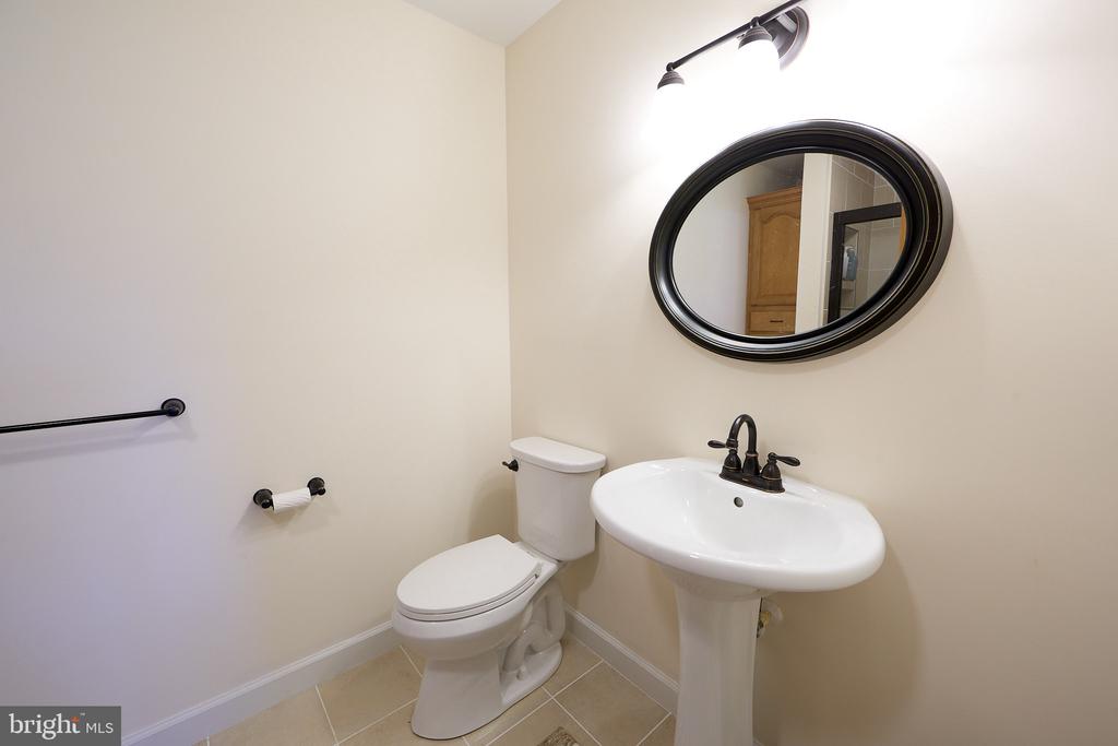 Half bathroom with a pedestal sink, oval black-framed mirror, and white toilet.