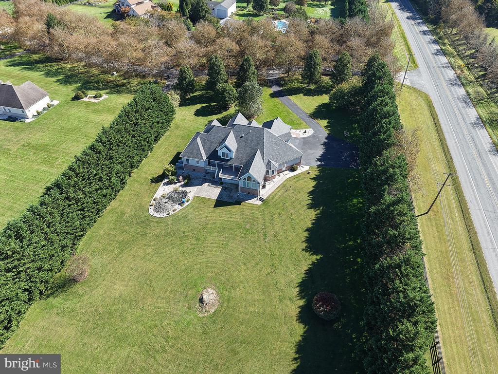 Aerial view of a detached house with a broad lawn, mature trees, and a paved driveway.