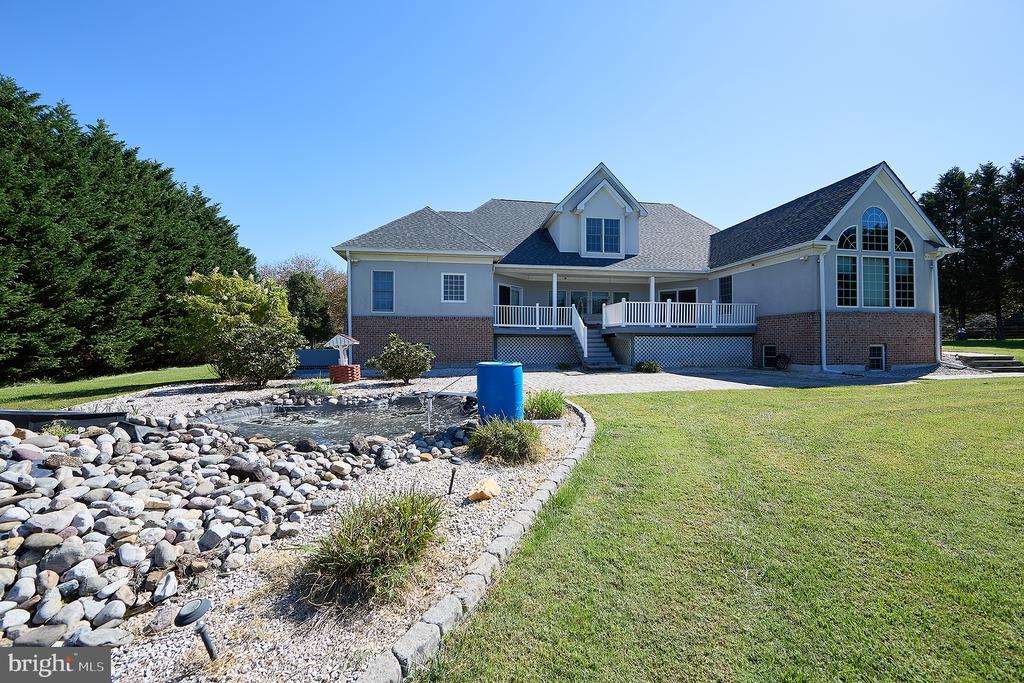 Rear of a two-story house with a raised deck, arched window, and rock-lined drainage swale.