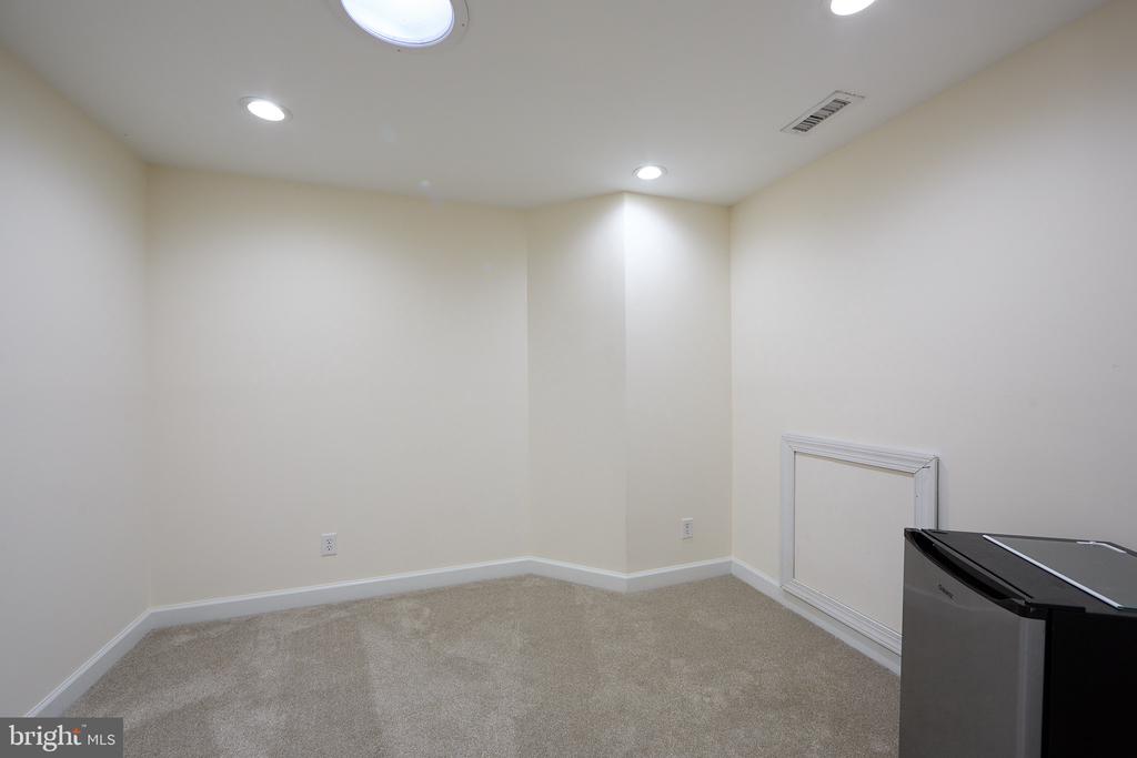 Empty carpeted room with recessed lights and a small wall access panel.