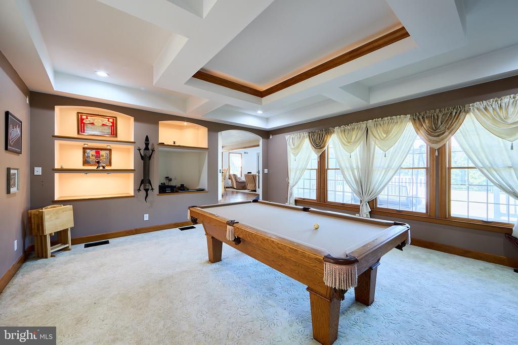 Billiard room with a wooden pool table, illuminated display shelves, and large curtained windows.