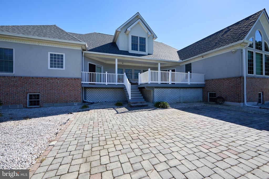 Rear of a gray and brick home with a raised deck and broad paved patio.