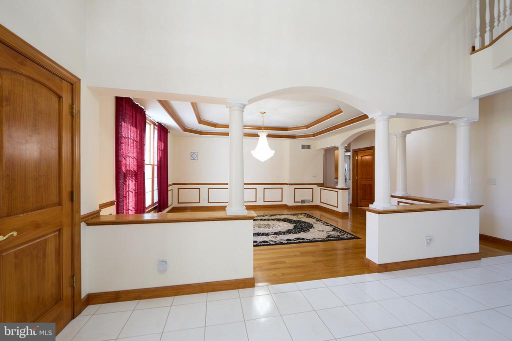 Open foyer leading into a hardwood-floored room with decorative columns, an arch, and red curtains.