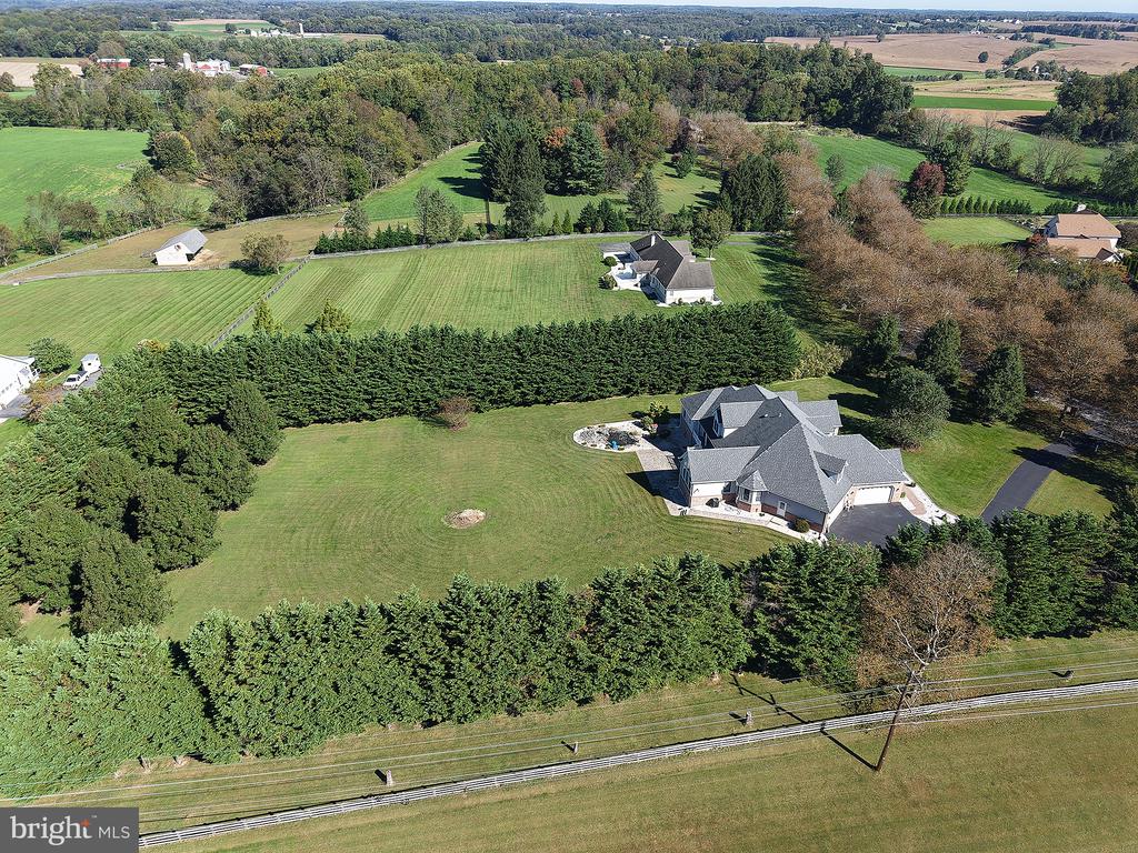 Aerial view of a large home with a broad lawn and dense evergreen hedges.