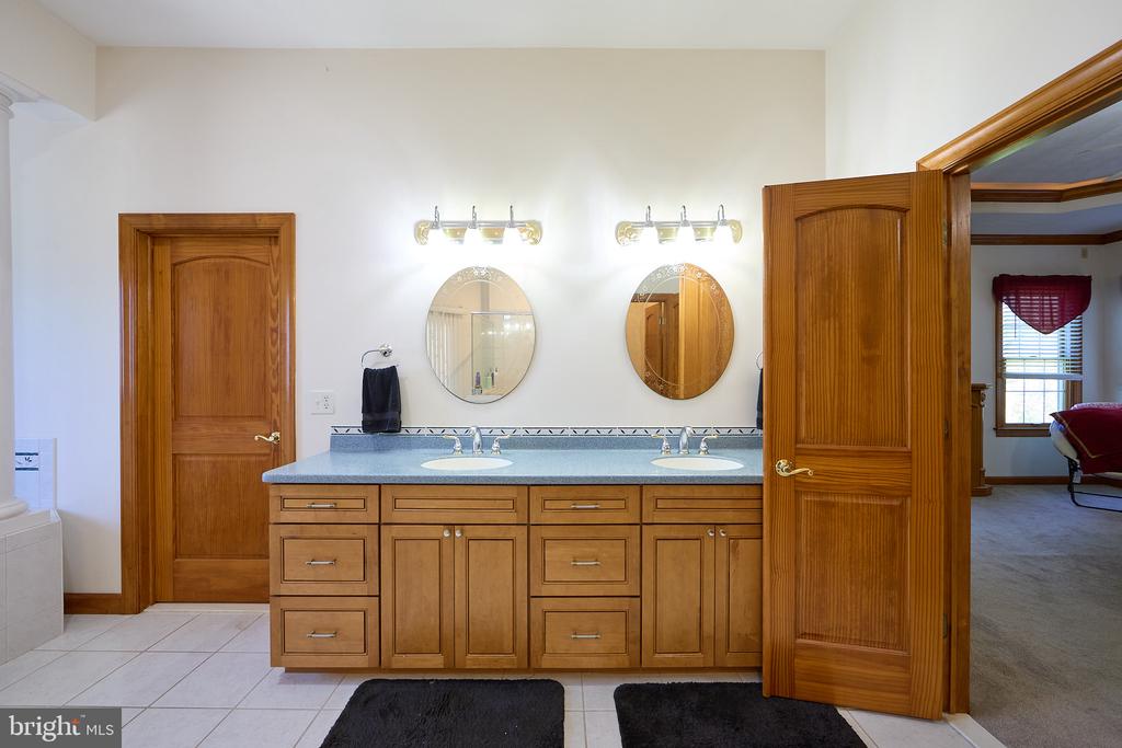 Bathroom with a double-sink wood vanity, oval mirrors, and an open door to a carpeted room.