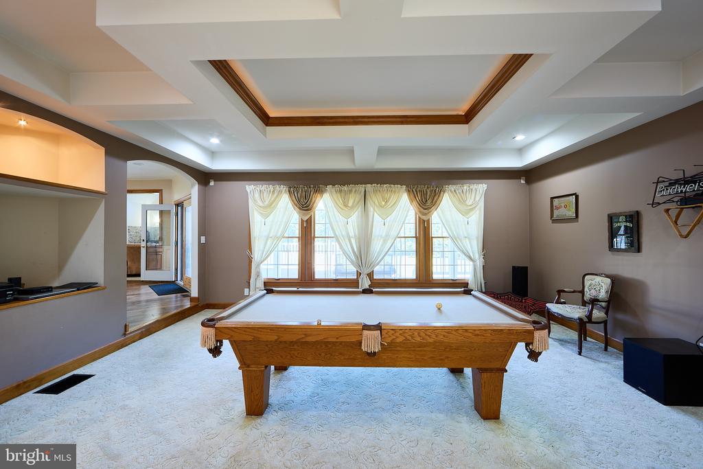 Billiard room with a wooden pool table, large curtained windows, and a tray ceiling.