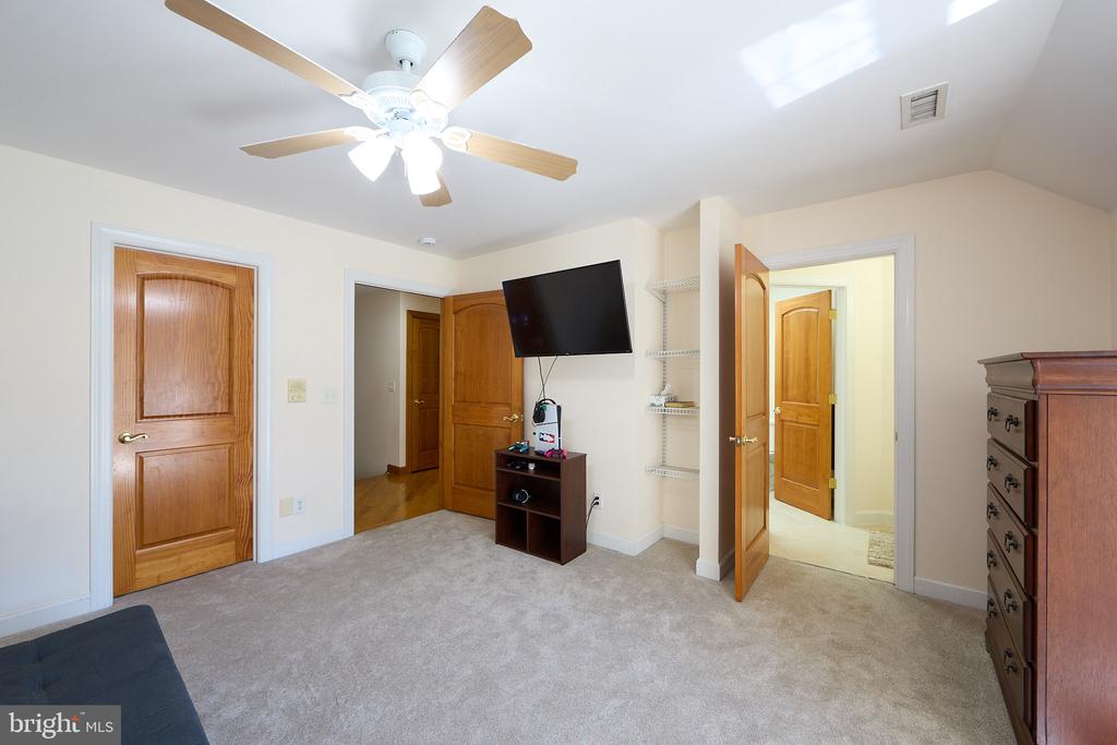 Carpeted bedroom with a ceiling fan, wall-mounted television, multiple wooden doors, and a dresser.