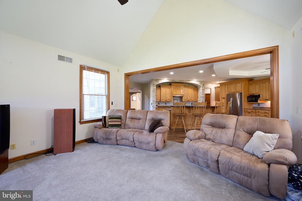 Living room with beige reclining sofas and carpet, opening into a kitchen with wood cabinetry.