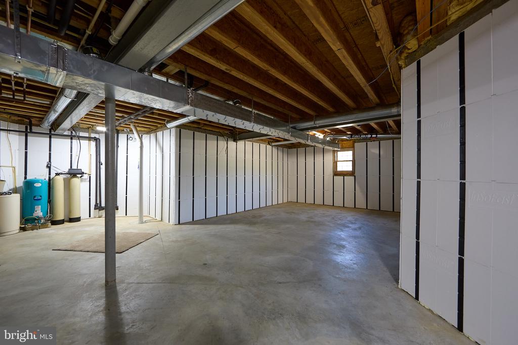 Unfinished basement with a concrete floor, exposed ceiling joists, insulated walls, and water-treatment equipment.