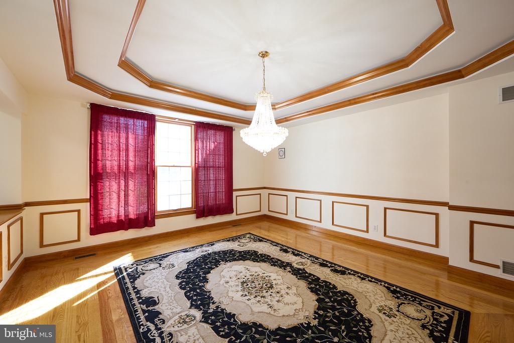 Bright room with a wood-trimmed tray ceiling, crystal chandelier, and patterned rug.