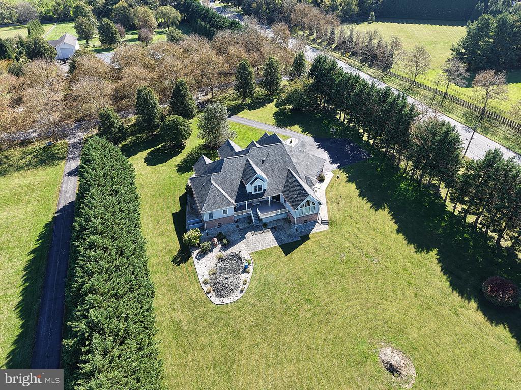 Aerial view of a large home surrounded by a broad lawn and rows of evergreen trees.