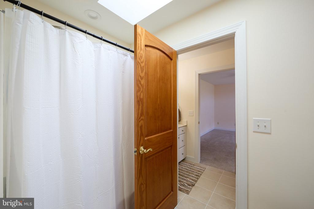 Bathroom with a white shower curtain and tiled floor, viewed through an open wooden door.