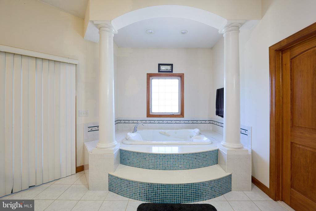 Bathroom with a built-in soaking tub, blue mosaic-tile steps, and white columns.