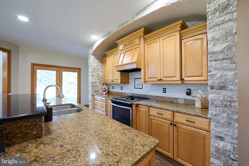 Kitchen with honey-colored cabinets, granite island, gas range, and stone-clad arch.