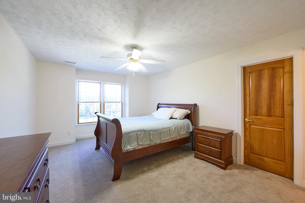 Bedroom with a dark wood bed, matching nightstand, ceiling fan, and two windows with blinds.