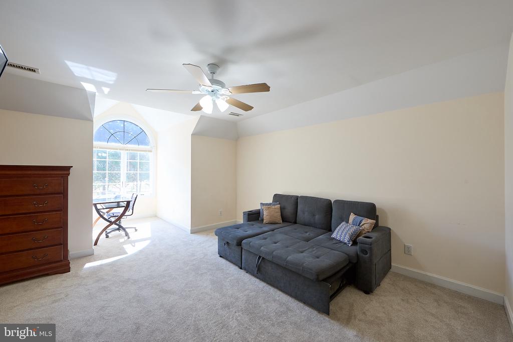 Furnished room with a gray sectional sofa and a desk beside a large arched window.