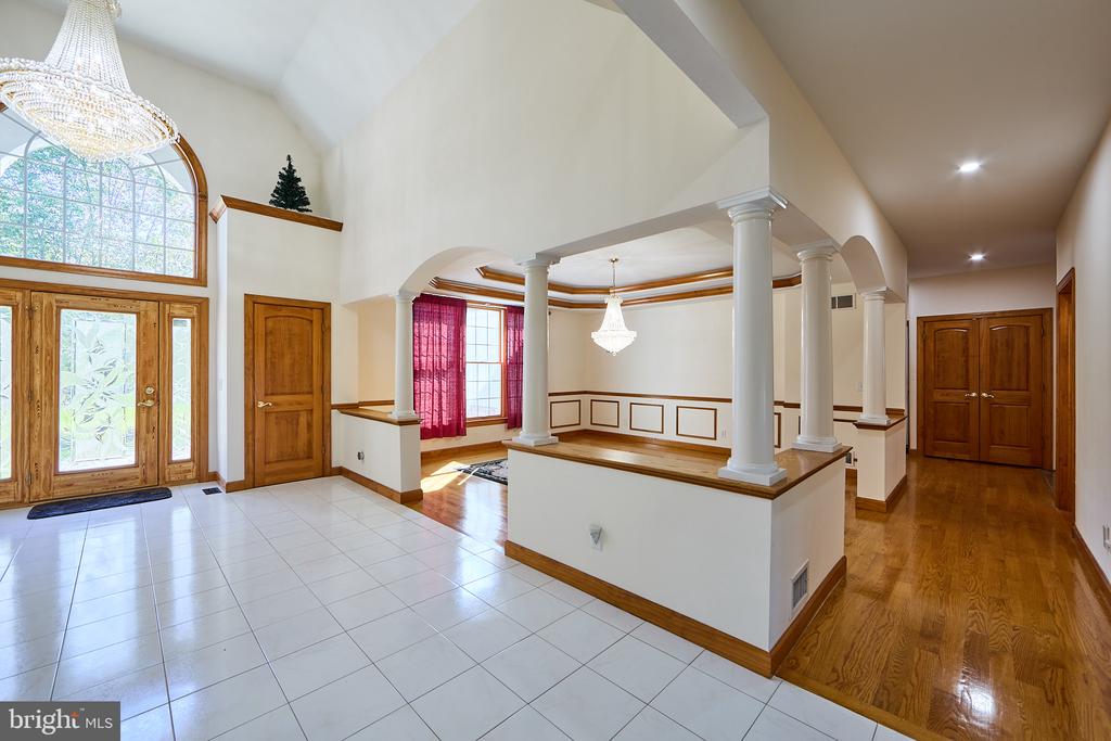 Two-story foyer with an arched glass entry, crystal chandelier, white columns, and hardwood hallway.