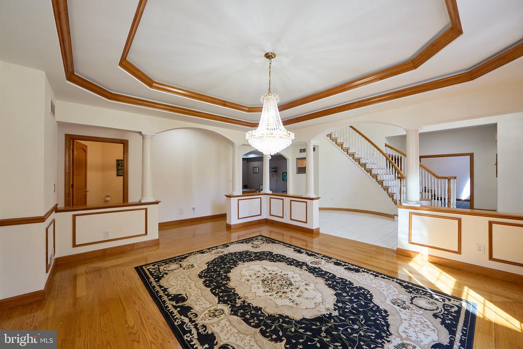 Spacious foyer with a crystal chandelier, wood-trimmed tray ceiling, hardwood floors, and staircase.