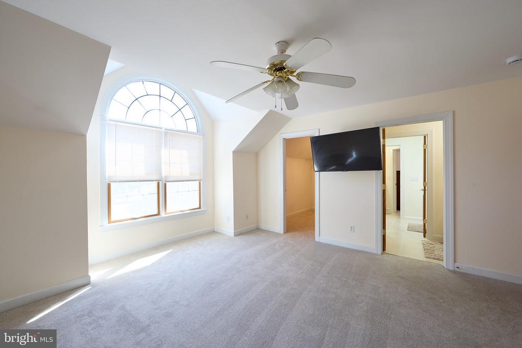 Empty carpeted bedroom with an arched window, ceiling fan, and wall-mounted television.