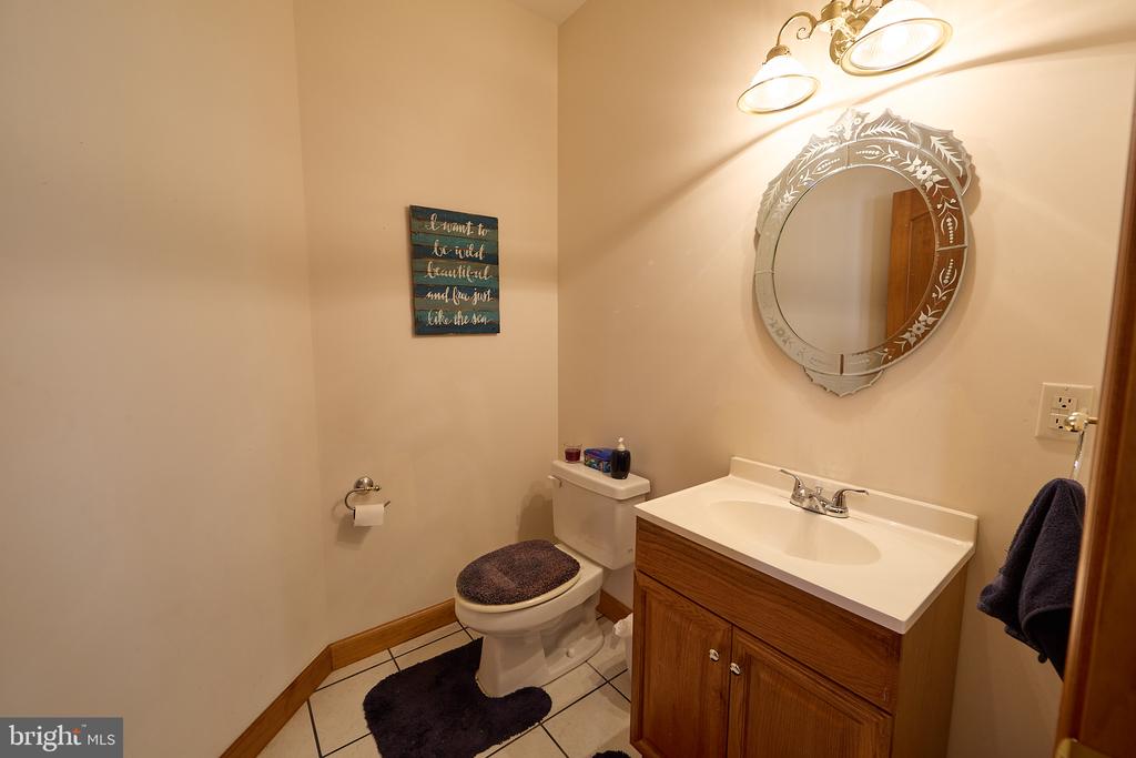 Bathroom with a wood vanity, white sink, ornate round mirror, and toilet.