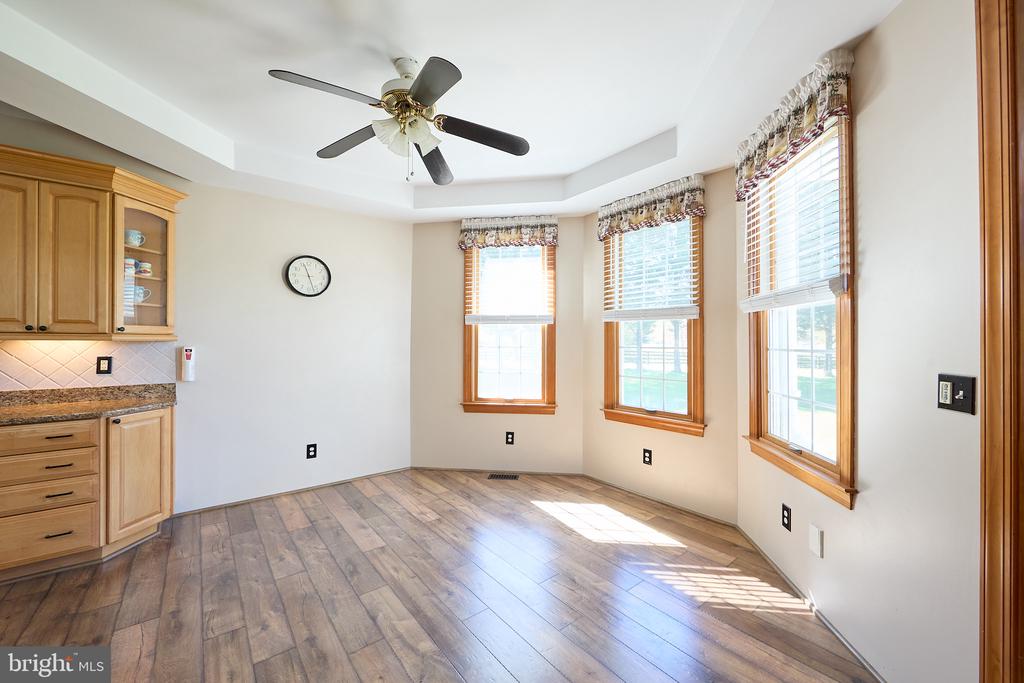 Dining nook with three tall windows, wood-look flooring, and kitchen cabinetry along one wall.