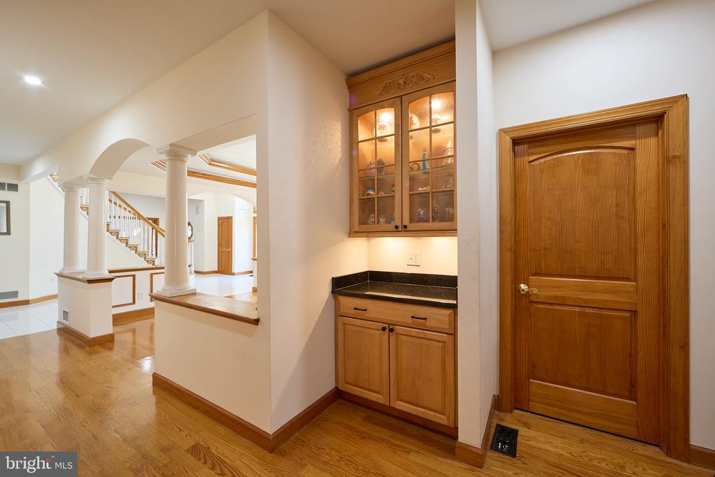 Foyer with hardwood floors, a columned staircase, built-in wood cabinetry, and a paneled wood door.