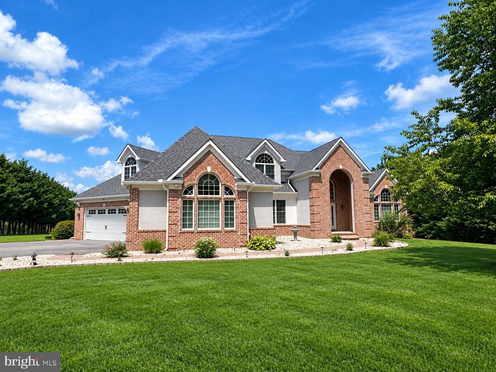 Brick-and-stucco home with an arched entrance, attached garage, and broad green lawn.