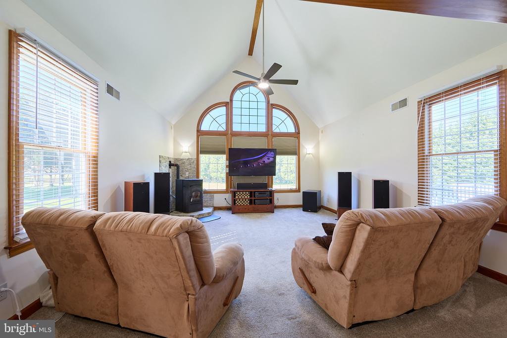 Furnished living room with vaulted ceiling, arched windows, fireplace, and tan recliners.