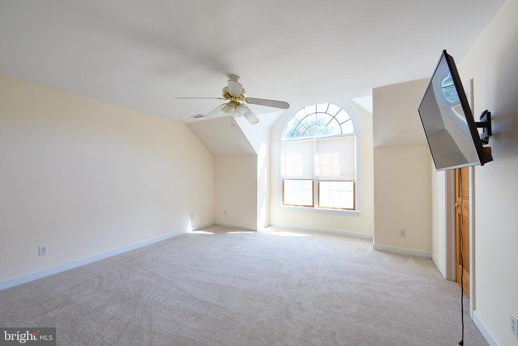 Empty carpeted room with an arched window, ceiling fan, and wall-mounted TV.