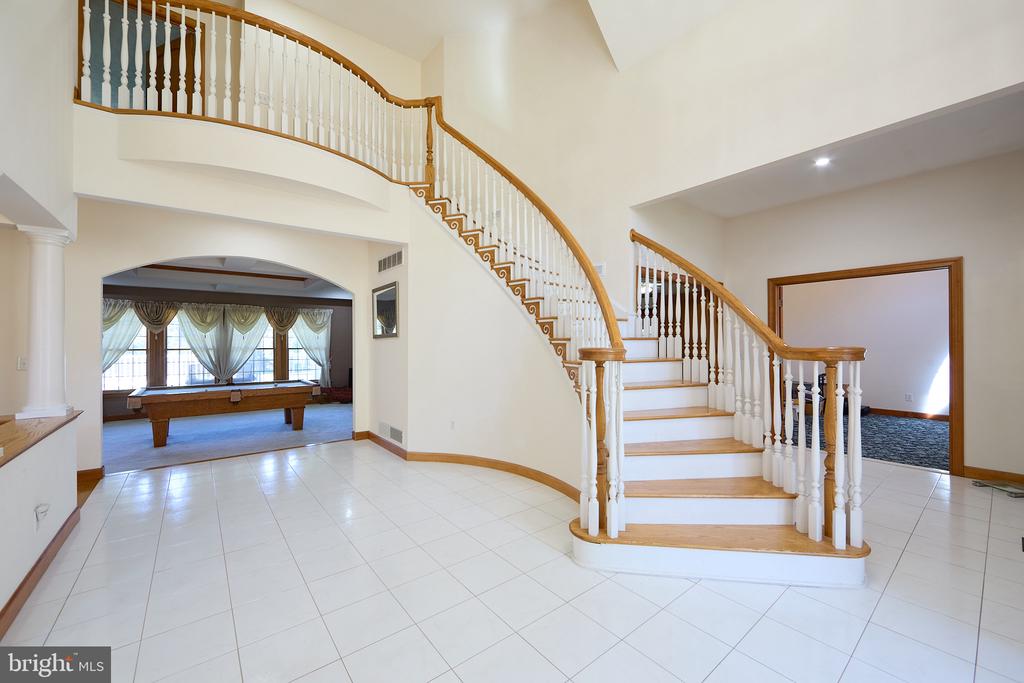 Foyer with a sweeping curved staircase, wood handrails, and an adjoining room with a pool table.