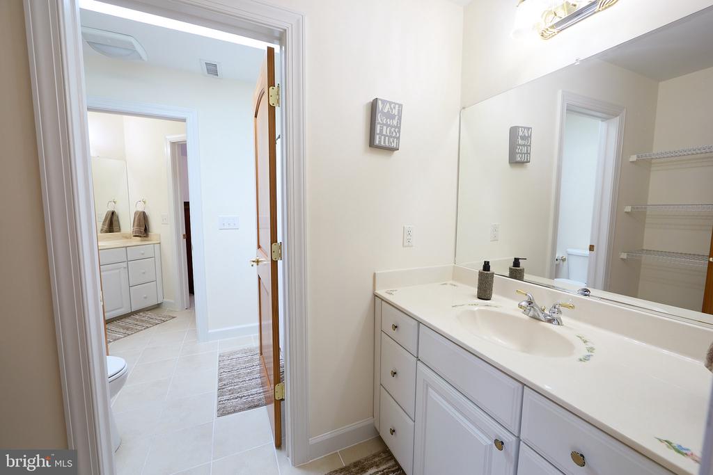 Bathroom vanity with white cabinetry and a large mirror, viewed toward an adjoining toilet area.