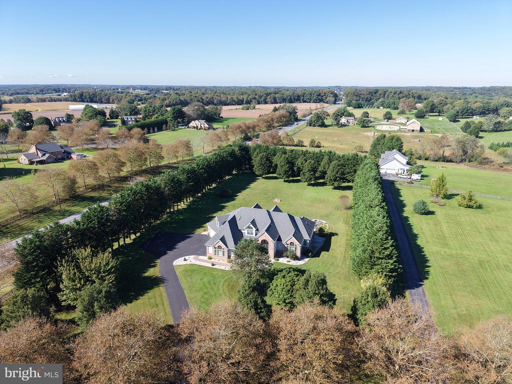 Aerial view of a home with a long driveway, broad lawn, and evergreen tree borders.