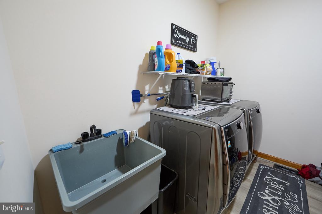 Laundry room with a deep utility sink, washer and dryer, and wall shelf of supplies.