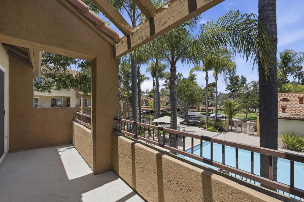 Balcony with a wooden pergola overlooking a swimming pool and palm-lined grounds.