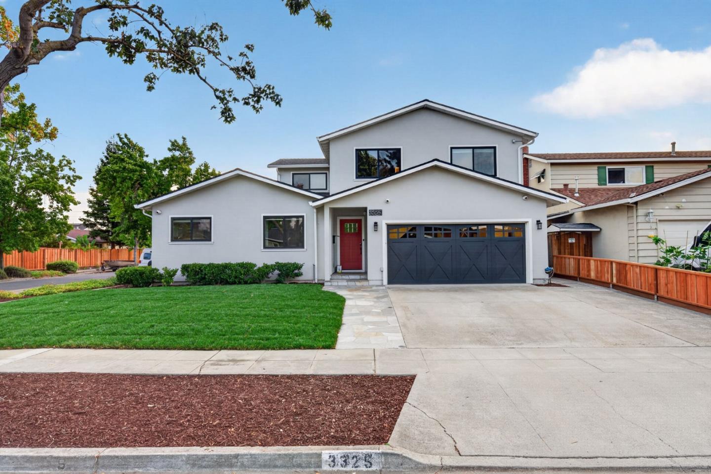 Two-story gray house with a red front door, dark double garage, and broad driveway.
