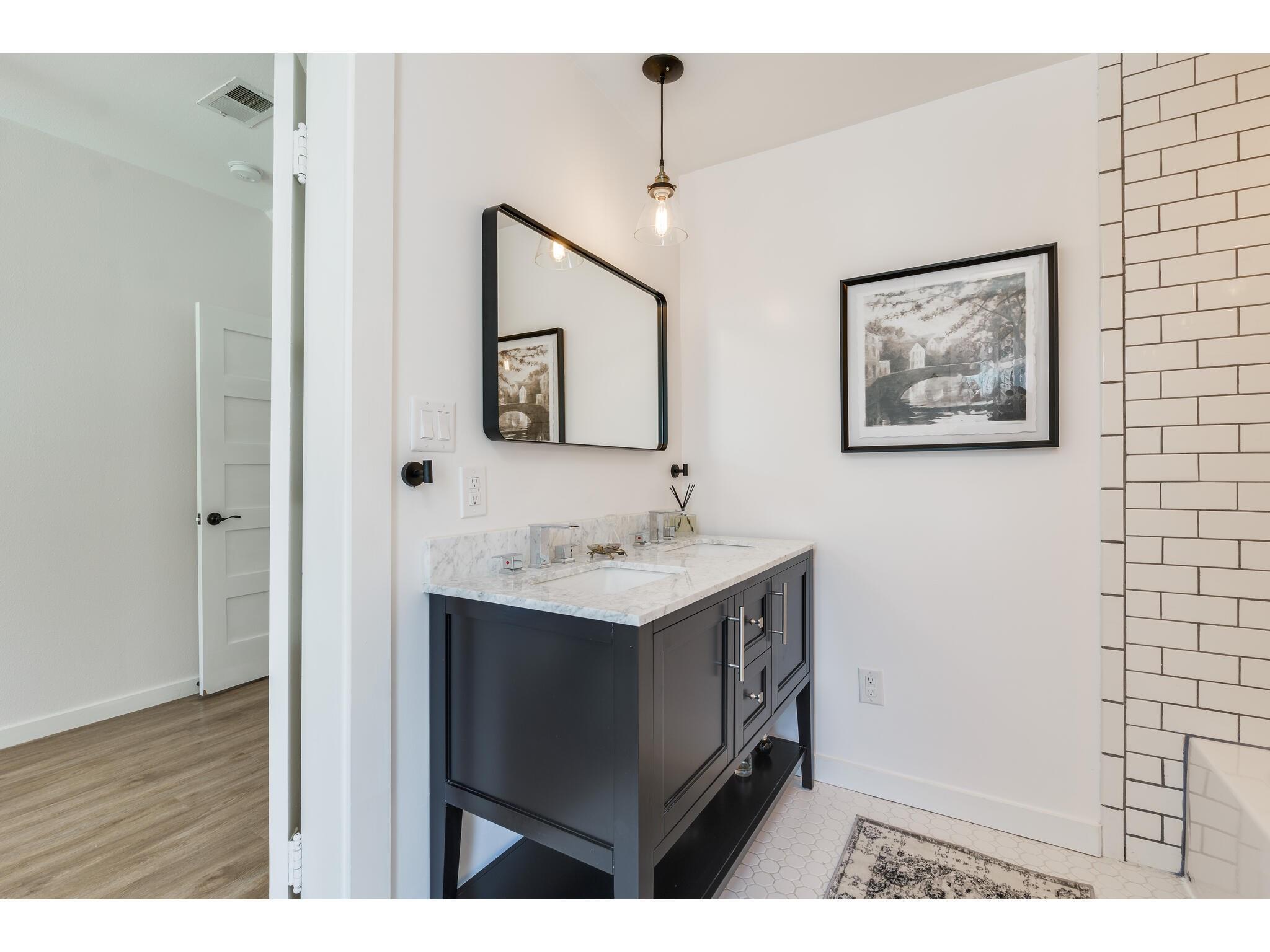 Bathroom with a dark vanity, marble countertop, large mirror, and white subway tile.
