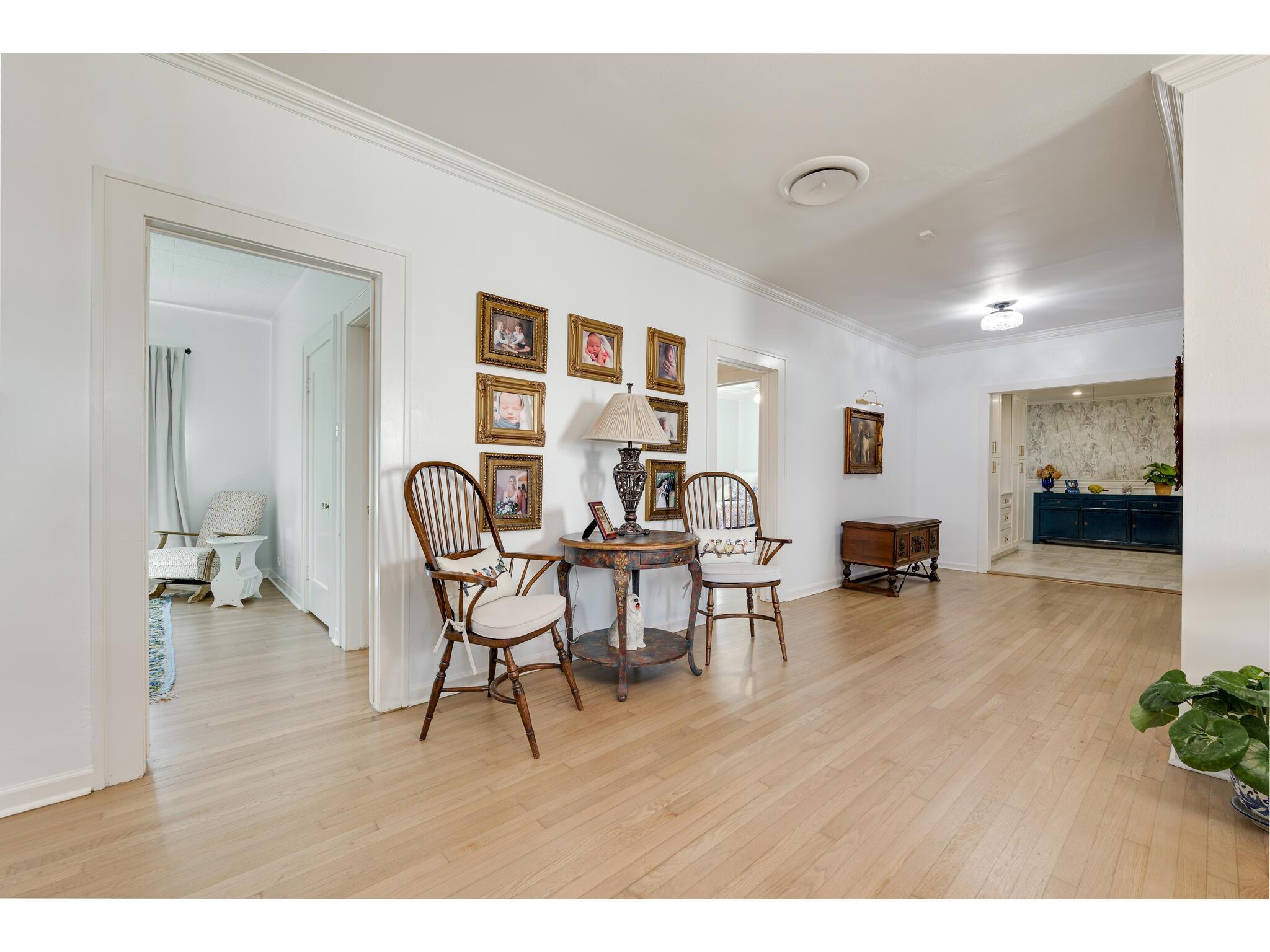 Furnished hallway with pale hardwood floors, a round table, wooden chairs, and framed photos.