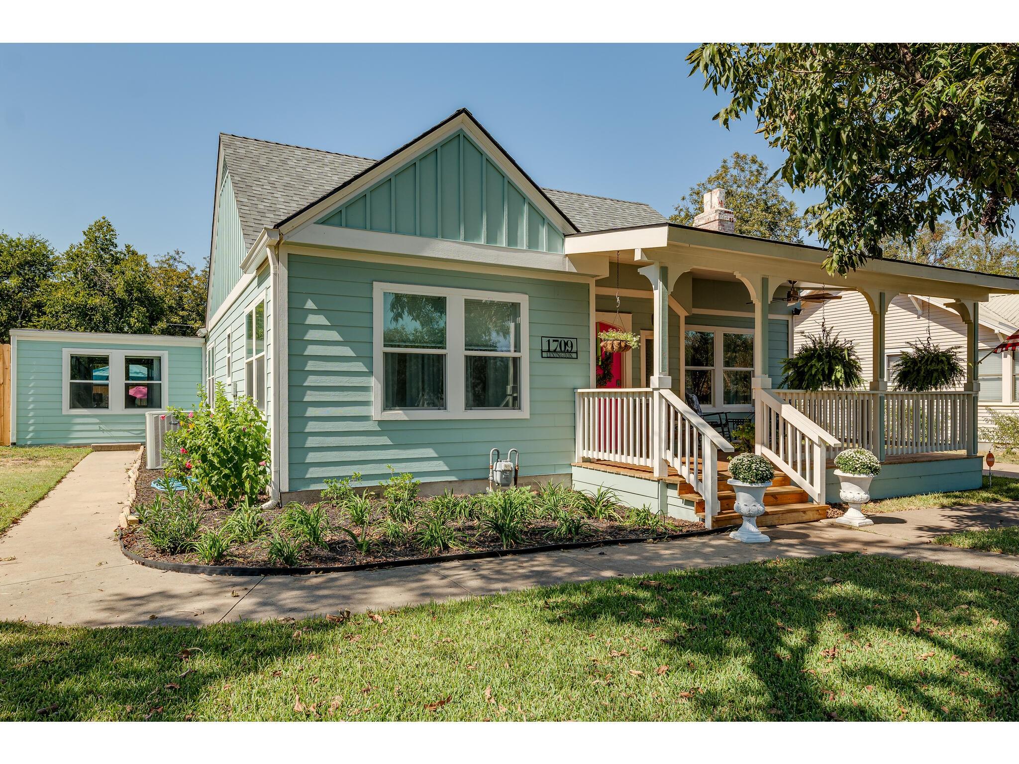 Light teal house with a covered porch, white railings, and landscaped front garden.