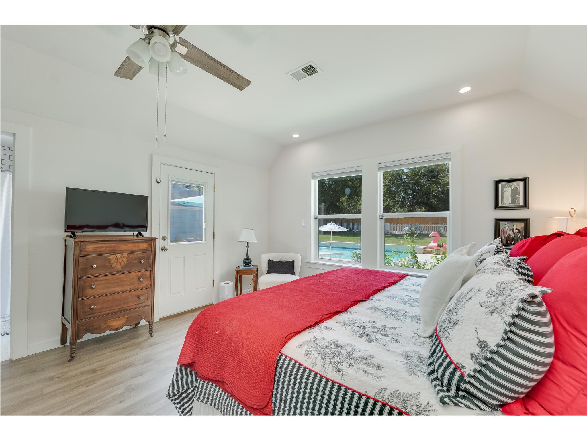 Bedroom with a red-covered bed and windows overlooking a backyard pool.