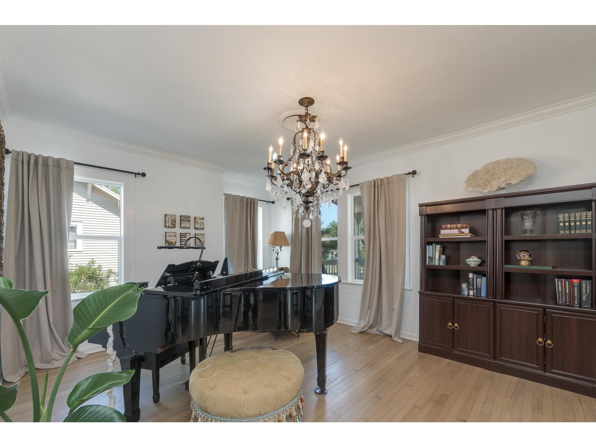 Music room with a black grand piano, crystal chandelier, and dark built-in bookcase.