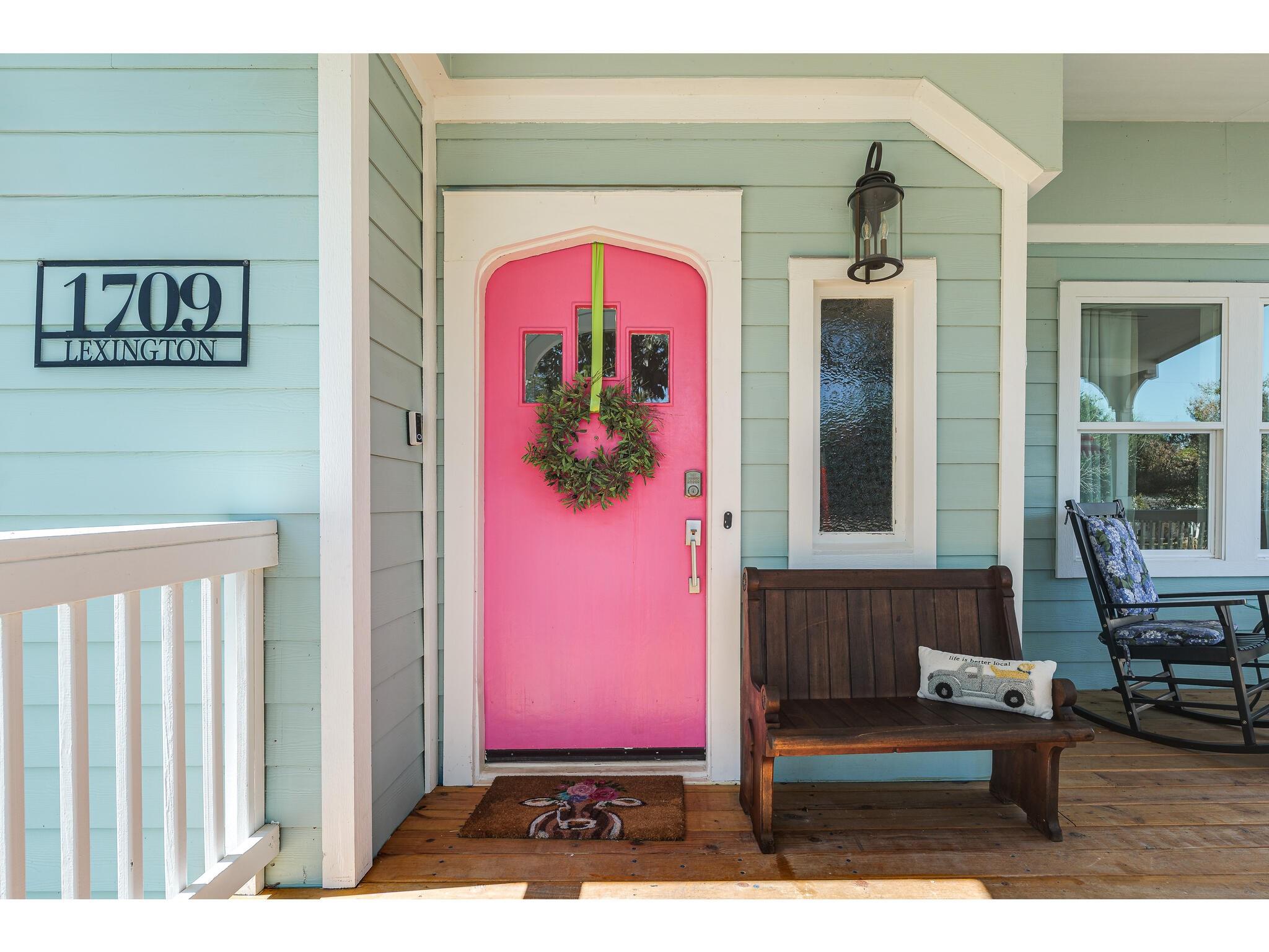 House front porch with a vivid pink wreath-adorned door, wooden bench, and 1709 Lexington sign.