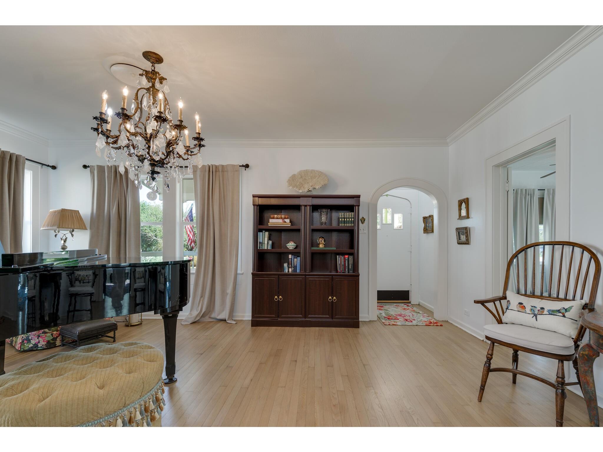 Living room with a black grand piano, crystal chandelier, and dark wood bookcase.