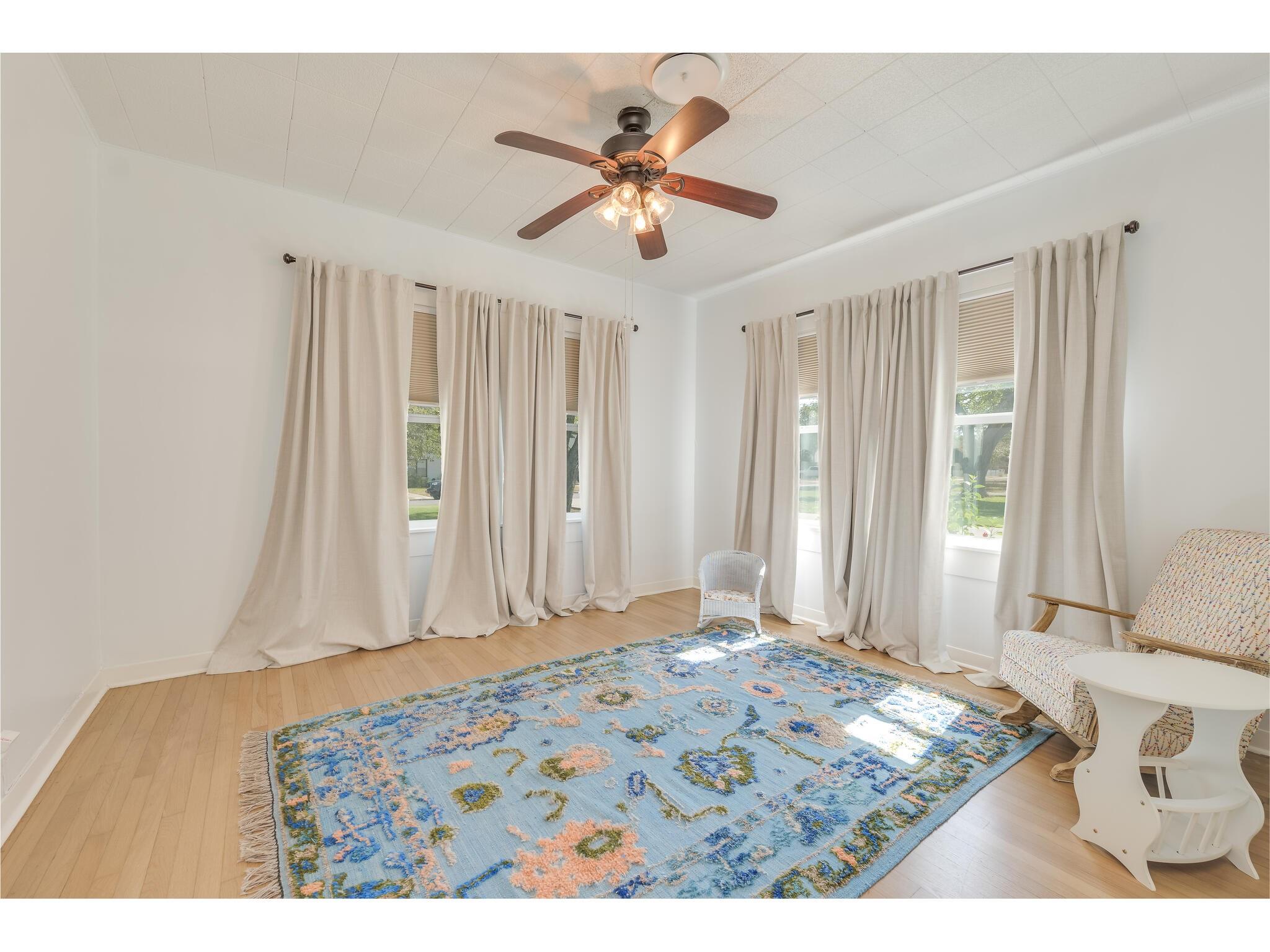 Bright room with tall curtained windows, a ceiling fan, and a blue floral rug.
