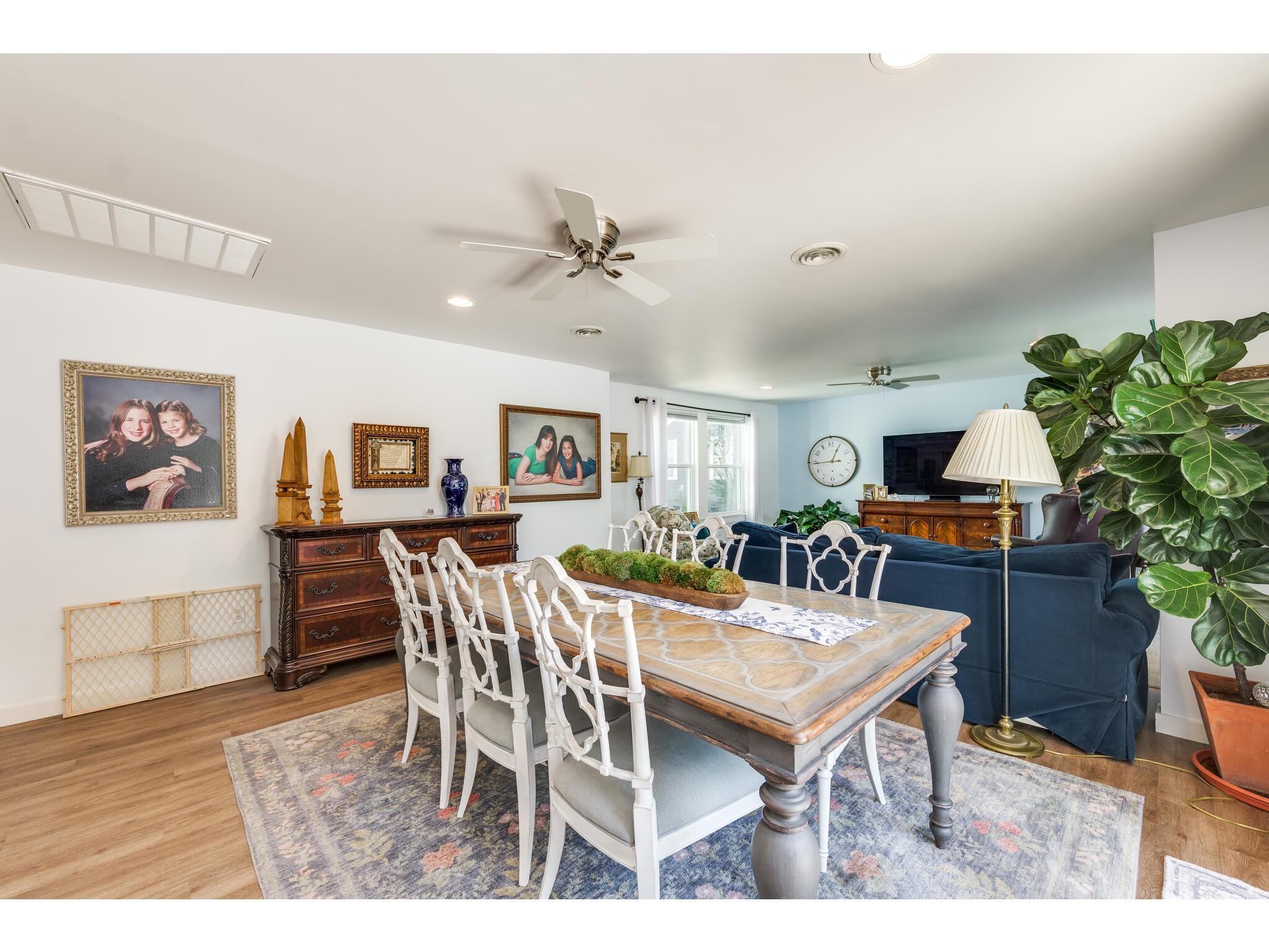 Dining area with a large wooden table and white chairs beside a blue sofa and leafy plant.