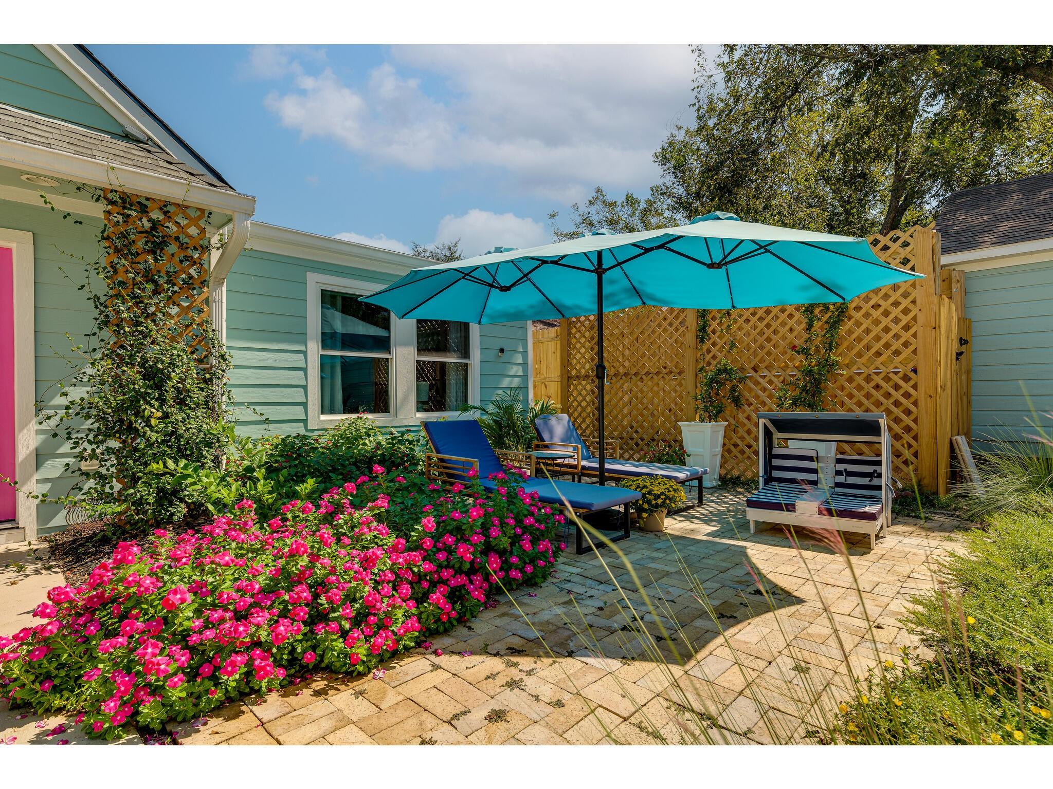 Backyard patio with a turquoise umbrella, lounge chairs, and bright pink flowers.